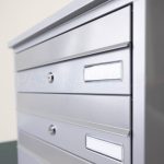 PD91_A sērijas ārtelpu sekciju pastkaste ar nosegvāciņiem un info plāksnītēm adreses vai saņēmēja informācijas norādīšanai. Pelēka pastkaste